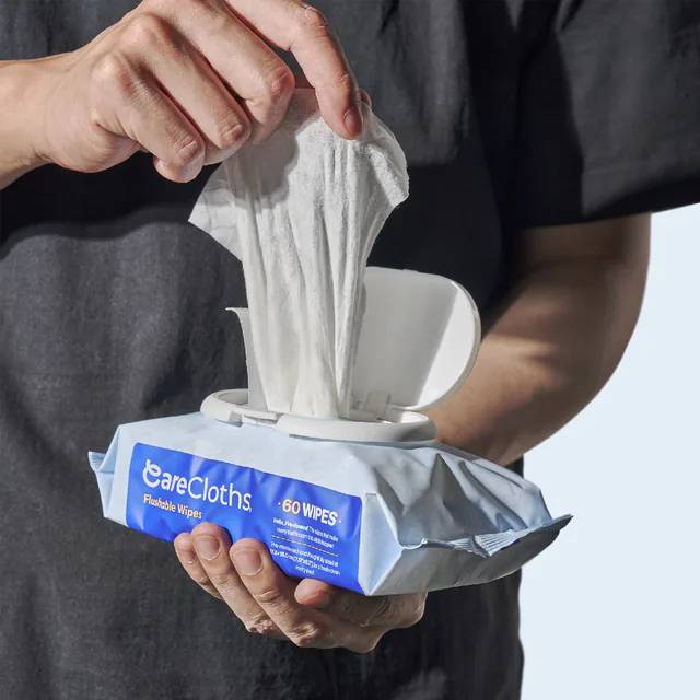 A hand pulling a single wipe from the push-to-open lid